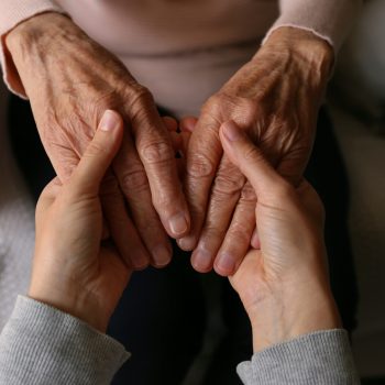 Cropped shot of elderly woman and female geriatric social worker holding hands. Women of different age comforting each other. Close up, background, copy space.