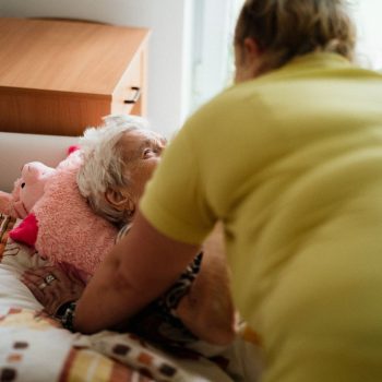 Nurse assisting elderly woman in a comfortable medical facility setting.